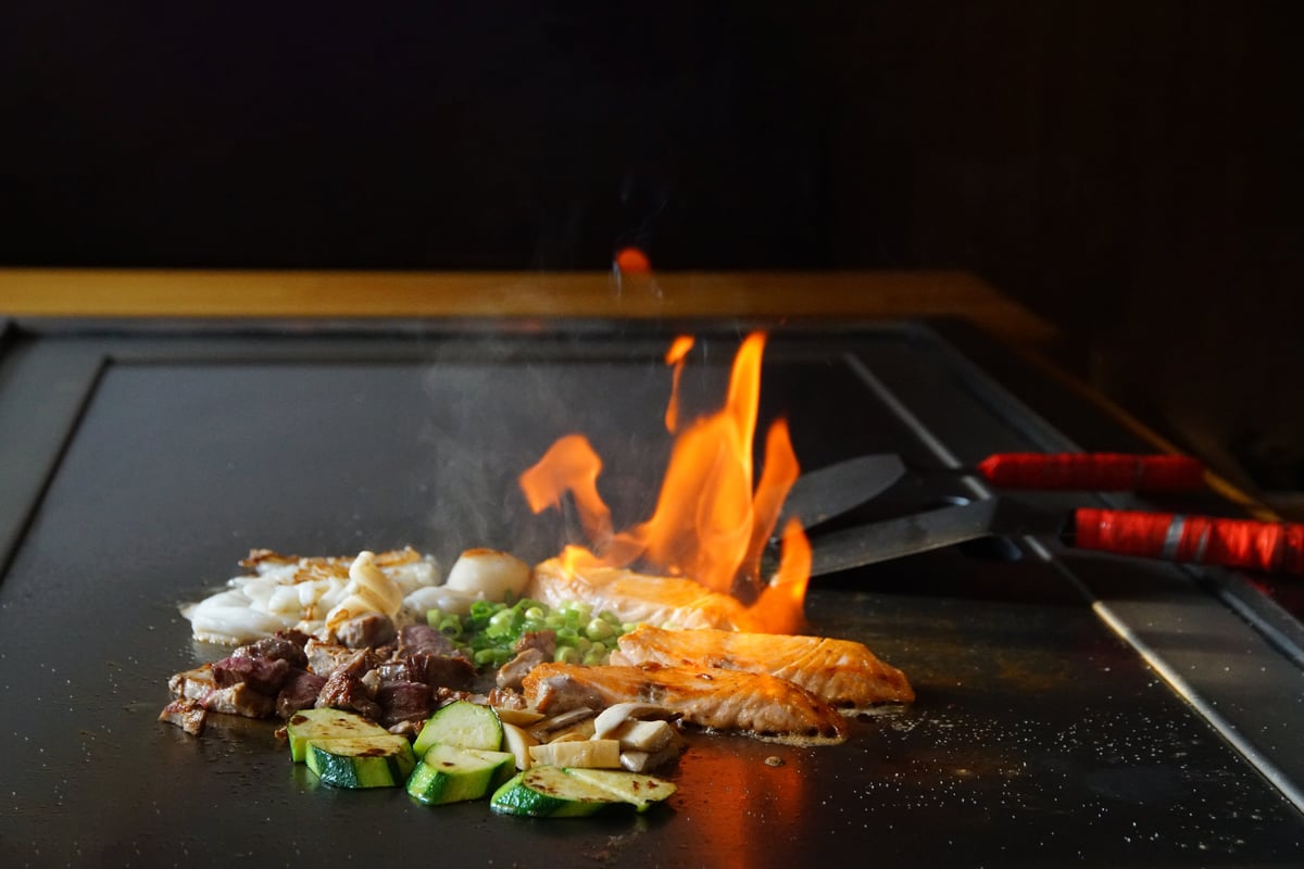 chef's hands with spatula over teppanyaki. cooking vegetables meat and seafood on hot hibachi grill table. Traditional Japanese Cuisine. Teppan show